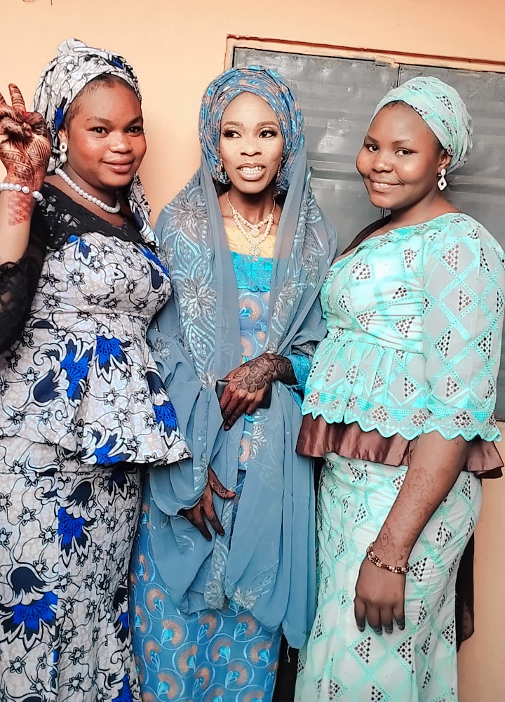 Three young women wearing coordinated blue outfits at a Nigerian ceremony